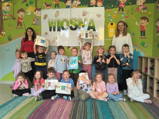 Grupowe zdjęcie pracownika ZPKWŚ z dziećmi z przedszkola. Dzieci trzymają kartki z informacją o segregacji śmieci.