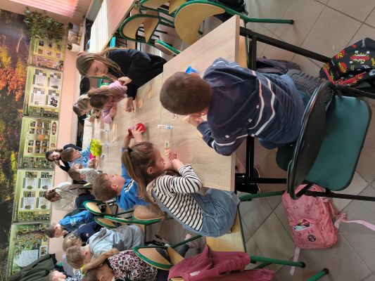 Dzieci siedzą przy stolikach i ozdabiają jajka wielkanocne z papieru.